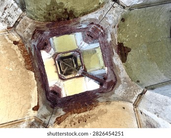 A dramatic low-angle view looking upward from inside the deteriorated vertical shaft of an abandoned structure, resembling an old church belfry or historic bell tower. Weathered walls, exposed architectural details, and the open shaft create a strong sense of decay, depth, history, and mystery. The perspective emphasizes the height and deteriorated condition of the forgotten building.