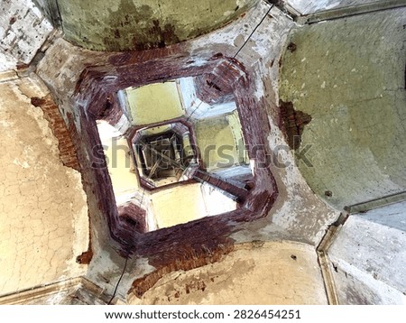 A dramatic low-angle view looking upward from inside the deteriorated vertical shaft of an abandoned structure, resembling an old church belfry or historic bell tower. Weathered walls, exposed architectural details, and the open shaft create a strong sense of decay, depth, history, and mystery. The perspective emphasizes the height and deteriorated condition of the forgotten building.