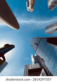 A dramatic low-angle view of modern skyscrapers in West Bay, Doha, Qatar, showcasing contemporary architecture and reflective glass towers against a vibrant blue sky. Captured from street level, the composition emphasizes the city’s impressive skyline, urban development, business district, and Middle Eastern metropolitan landscape. Ideal for concepts related to architecture, finance, tourism, real estate, and modern city life.