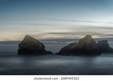 Dramatic low-angle view of rugged sea stacks rising from ethereal ocean under muted evening light.