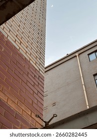 A dramatic low-angle view of two adjoining brick building walls with different colors—red and beige—highlighting symmetry, contrast, and urban architecture. Captured under a clear blue sky, this minim