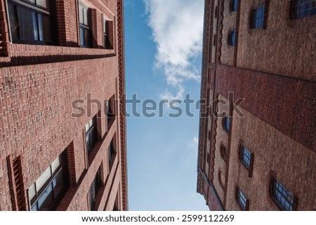 A dramatic low-angle view of two historic brick buildings converging towards the sky. 