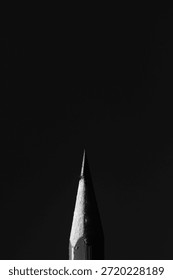 Dramatic low-key macro of a pencil tip emerging from total darkness. Stark lighting highlights the texture of the wood and graphite, ideal for concepts of ideas, inspiration, and mystery.
