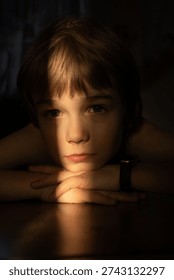 dramatic, low-key portrait of a child. The light highlights the details of the face. Close-up of the boy's face. Sadness, longing, mental health, concentration. Anxiety and anticipation