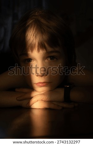 dramatic, low-key portrait of a child. The light highlights the details of the face. Close-up of the boy's face. Sadness, longing, mental health, concentration. Anxiety and anticipation