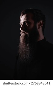 Dramatic low-key profile portrait of a bearded man lit from the side in a dark studio. Moody, contemplative expression and textured facial hair create a cinematic, masculine headshot for editorial use.