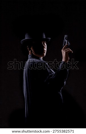 Dramatic low-light portrait of a person in a hat holding a handgun upright, partially turned toward the viewer. Strong shadows and contrast create a cinematic noir mood with copy space