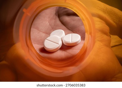Dramatic macro view looking from the inside of an empty, bright orange prescription pill bottle. A human hand is visible reaching a small dose of tablets.