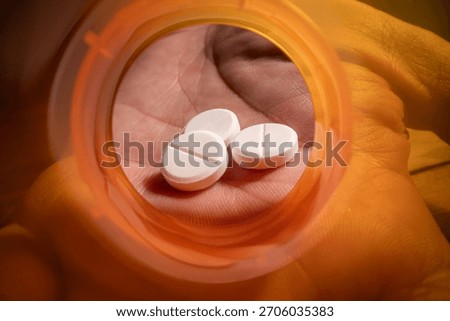 Dramatic macro view looking from the inside of an empty, bright orange prescription pill bottle. A human hand is visible reaching a small dose of tablets.