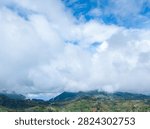 Dramatic massive white clouds over green terraced agricultural hills and mountain range