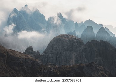 A dramatic, mist-covered landscape view of the rugged, jagged peaks of Cadini di Misurina in the Italian Dolomites.
