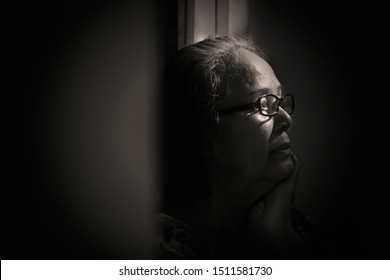 Dramatic Monochrome Lowkey Portrait Of 60s Or 70s A Sian Old Lady In The Light And Shadow. Granny With Eyeglass  Sitting In The Dark Corner And L Flew Away.Sad Elderly Senior Woman Concept.
