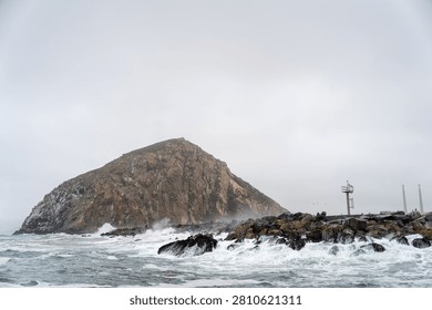 Dramatic Morro Rock Volcanic Plug Shrouded in Cloudy Weather and Coastal Fog, Morro Bay, California