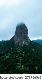 Dramatic mountain landscape featuring Pedra do Baú rising above dense fog and low clouds in the Serra da Mantiqueira region of southeastern Brazil. The massive rock formation dominates the scenery with steep walls and rugged terrain surrounded by forested hills and elevated peaks. Soft diffused light filters through mist covering the mountains, creating a cinematic atmosphere associated with adventure, exploration and remote highland environments.

The location is widely recognized for climbing, hiking and mountaineering activities, attracting visitors seeking outdoor experiences and panoramic views above the clouds. Trails crossing the mountainsides reveal changing weather conditions typical of high elevation regions, where fog and moving clouds constantly transform the scenery. The combination of dramatic relief, natural textures and expansive horizons creates a visually striking environment connected with ecotourism and adventure travel.

This scene was photographed at Pedra do Baú in the Serra da Mantiqueira, a famous destination in Brazil admired for rock climbing routes, mountain landscapes and scenic viewpoints surrounded by preserved nature in South America.