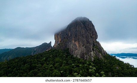 Dramatic mountain landscape featuring Pedra do Baú rising above dense fog and low clouds in the Serra da Mantiqueira region of southeastern Brazil. The massive rock formation dominates the scenery with steep walls and rugged terrain surrounded by forested hills and elevated peaks. Soft diffused light filters through mist covering the mountains, creating a cinematic atmosphere associated with adventure, exploration and remote highland environments.

The location is widely recognized for climbing, hiking and mountaineering activities, attracting visitors seeking outdoor experiences and panoramic views above the clouds. Trails crossing the mountainsides reveal changing weather conditions typical of high elevation regions, where fog and moving clouds constantly transform the scenery. The combination of dramatic relief, natural textures and expansive horizons creates a visually striking environment connected with ecotourism and adventure travel.

This scene was photographed at Pedra do Baú in the Serra da Mantiqueira, a famous destination in Brazil admired for rock climbing routes, mountain landscapes and scenic viewpoints surrounded by preserved nature in South America.