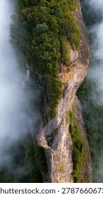 Dramatic mountain landscape featuring Pedra do Baú rising above dense fog and low clouds in the Serra da Mantiqueira region of southeastern Brazil. The massive rock formation dominates the scenery with steep walls and rugged terrain surrounded by forested hills and elevated peaks. Soft diffused light filters through mist covering the mountains, creating a cinematic atmosphere associated with adventure, exploration and remote highland environments.

The location is widely recognized for climbing, hiking and mountaineering activities, attracting visitors seeking outdoor experiences and panoramic views above the clouds. Trails crossing the mountainsides reveal changing weather conditions typical of high elevation regions, where fog and moving clouds constantly transform the scenery. The combination of dramatic relief, natural textures and expansive horizons creates a visually striking environment connected with ecotourism and adventure travel.

This scene was photographed at Pedra do Baú in the Serra da Mantiqueira, a famous destination in Brazil admired for rock climbing routes, mountain landscapes and scenic viewpoints surrounded by preserved nature in South America.