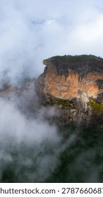Dramatic mountain landscape featuring Pedra do Baú rising above dense fog and low clouds in the Serra da Mantiqueira region of southeastern Brazil. The massive rock formation dominates the scenery with steep walls and rugged terrain surrounded by forested hills and elevated peaks. Soft diffused light filters through mist covering the mountains, creating a cinematic atmosphere associated with adventure, exploration and remote highland environments.

The location is widely recognized for climbing, hiking and mountaineering activities, attracting visitors seeking outdoor experiences and panoramic views above the clouds. Trails crossing the mountainsides reveal changing weather conditions typical of high elevation regions, where fog and moving clouds constantly transform the scenery. The combination of dramatic relief, natural textures and expansive horizons creates a visually striking environment connected with ecotourism and adventure travel.

This scene was photographed at Pedra do Baú in the Serra da Mantiqueira, a famous destination in Brazil admired for rock climbing routes, mountain landscapes and scenic viewpoints surrounded by preserved nature in South America.