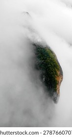 Dramatic mountain landscape featuring Pedra do Baú rising above dense fog and low clouds in the Serra da Mantiqueira region of southeastern Brazil. The massive rock formation dominates the scenery with steep walls and rugged terrain surrounded by forested hills and elevated peaks. Soft diffused light filters through mist covering the mountains, creating a cinematic atmosphere associated with adventure, exploration and remote highland environments.

The location is widely recognized for climbing, hiking and mountaineering activities, attracting visitors seeking outdoor experiences and panoramic views above the clouds. Trails crossing the mountainsides reveal changing weather conditions typical of high elevation regions, where fog and moving clouds constantly transform the scenery. The combination of dramatic relief, natural textures and expansive horizons creates a visually striking environment connected with ecotourism and adventure travel.

This scene was photographed at Pedra do Baú in the Serra da Mantiqueira, a famous destination in Brazil admired for rock climbing routes, mountain landscapes and scenic viewpoints surrounded by preserved nature in South America.