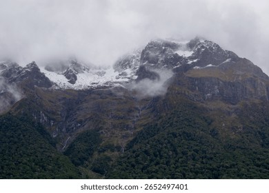 A dramatic mountain landscape shrouded in clouds, featuring snow-capped peaks and lush green forests at the base. The scene conveys a sense of mystery and natural beauty. - Powered by Shutterstock - Get 15% off with code: PIKWIZARD15