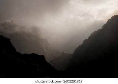 Dramatic mountain landscape with sunlight breaking through clouds, creating a mystical atmosphere.