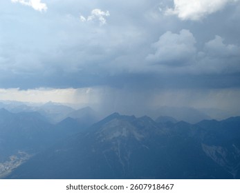 A dramatic mountain landscape under a cloudy sky, with dark clouds gathering and rain visible in the distance.