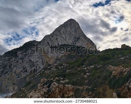 Dramatic mountain peak beneath brooding clouds, jagged silhouette and turbulent sky create tense atmosphere