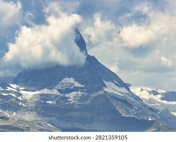 Dramatic mountain peak partially obscured by clouds, with snow-capped slopes. Serene, natural setting