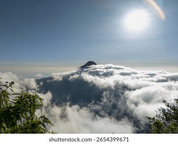 A dramatic mountain peak piercing through a vast sea of clouds under a brilliant sun, captured from a high vantage point. Excellent for inspirational travel and majestic nature themes.