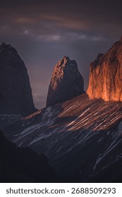 Dramatic mountain peaks at sunset with warm light casting shadows, showcasing nature's beauty and rugged landscape.