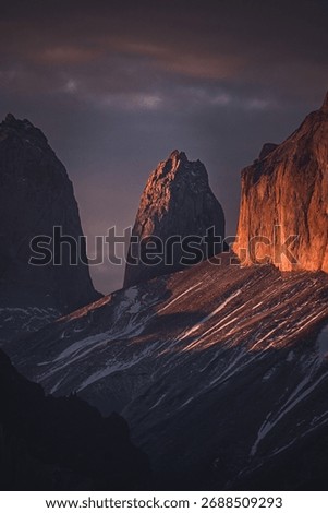 Dramatic mountain peaks at sunset with warm light casting shadows, showcasing nature's beauty and rugged landscape.