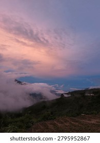 Dramatic mountain range landscape above the clouds during a colorful golden hour sunset.
