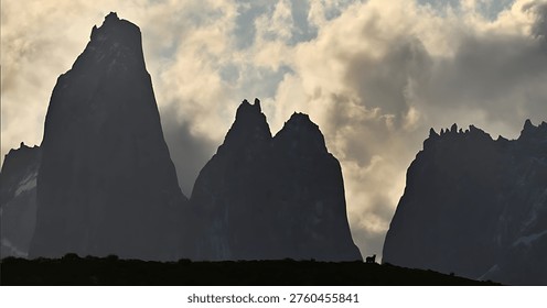 A dramatic mountain range silhouetted against a cloudy sky at sunset, showcasing the rugged terrain and majestic grandeur of nature's scenic beauty.
