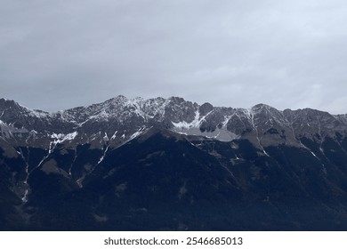 Dramatic Mountain Range with Snow-Capped Peaks Under a Moody Overcast Sky - Powered by Shutterstock