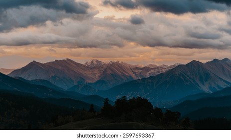 Dramatic mountain range at sunset under a cloudy sky. Deep shadows and warm light create a stunning landscape