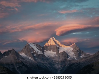 A dramatic mountain range under a vibrant sunset sky, with the highest peak illuminated by warm, golden light.