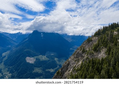 Dramatic mountain ridge and cloud-covered peaks above a dense evergreen forest and valley near Hope, British Columbia, Canada, evoking serenity and adventure.