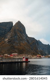Dramatic mountain rising above a small coastal village and calm harbor under a cloudy sky