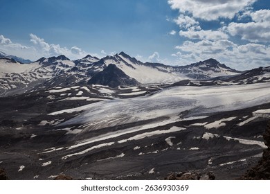 Dramatic mountain terrain features rugged peaks and expansive glaciers under a cloud-dotted sky. icy landscape reflects sunlight, highlighting the natural beauty of this remote region.