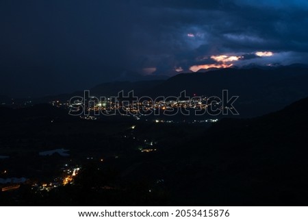 Dramatic night image of San Jose de Ocoa, Dominican Republic at sunset, with city lights in the valley and stormy skies.