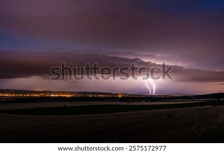 A dramatic night landscape featuring a vivid lightning strike over a distant illuminated city, under a moody cloudy sky.