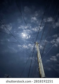 Dramatic night sky with bright moonlight shining through clouds, electric utility pole and power lines creating geometric patterns in urban area. Perfect for concepts of connection, infrastructure, nighttime, and calm atmosphere.