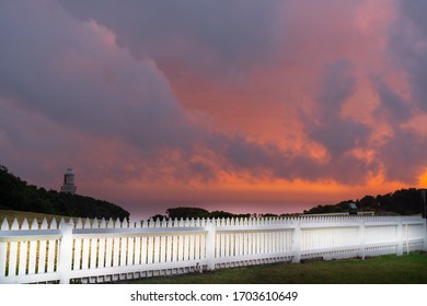 Dramatic Night Sky Red And Grey Clouds With Lighthouse In Distance Beyond White Picket Fence At The Cape Otway Lightstation,  Victoria Australia.