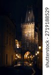 Dramatic night view of the Powder Tower (Prašná brána) in Prague, Czech Republic, illuminated by warm glowing street lights, moody and atmospheric evening. 