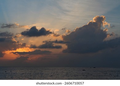 A dramatic ocean sunset with thick, towering clouds illuminated by the fading sunlight. The golden and orange hues peek through the edges of the clouds, casting a warm glow across the sky.