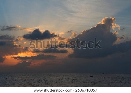 A dramatic ocean sunset with thick, towering clouds illuminated by the fading sunlight. The golden and orange hues peek through the edges of the clouds, casting a warm glow across the sky.