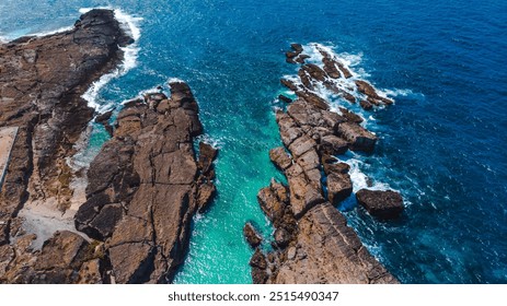 Dramatic ocean waves break against rocky shore, turquoise water shimmering in sunlight - Powered by Shutterstock