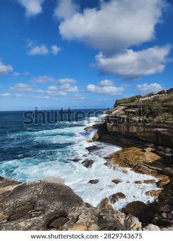 Dramatic ocean waves crash against rugged sandstone cliffs along the scenic Bondi to Coogee coastal walk in Sydney, Australia. Clear blue waters, sea foam, and bright skies create a beautiful natural landscape, perfect for coastal adventure travel.