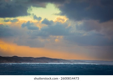 Dramatic opening in storm clouds showing blue sky with land an d sea below.