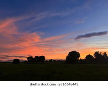 A dramatic orange and pink sunset sky over a dark rural field silhouette.