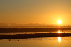 Dramatic Orange Sunrise In The Morning Over Water With Reflection Of The Sun On The Water At Bolsa Chica Ecological Reserve California, USA